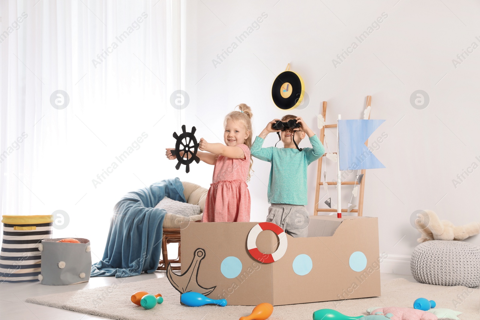 Photo of Cute little children playing with cardboard ship at home