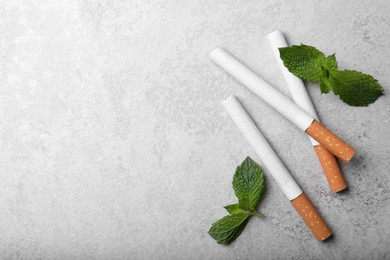 Photo of Menthol cigarettes and mint leaves on grey table, flat lay. Space for text