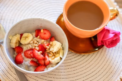 Photo of Delicious oatmeal with banana, strawberries, nuts and cup of hot drink on table, above view