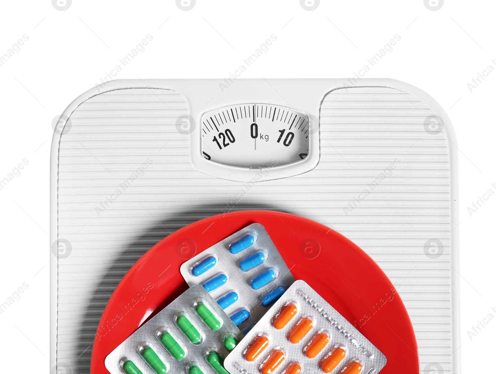 Photo of Scales with plate full of weight loss pills in blister packs on white background