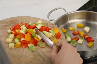 Woman putting cut vegetables into saute pan in kitchen, closeup