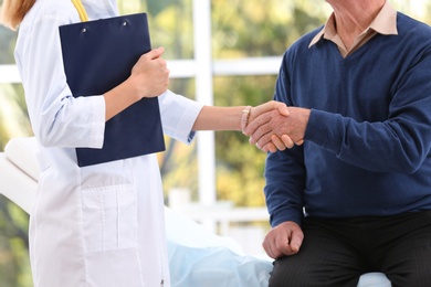Photo of Doctor and elderly patient shaking hands in hospital, closeup
