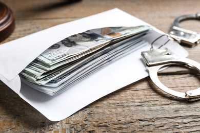 Dollar bills and handcuffs on wooden table, closeup. Bribe concept