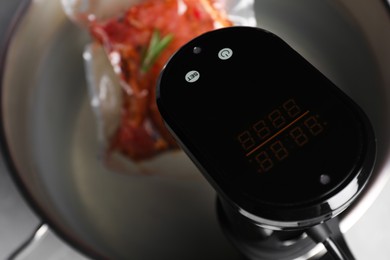 Photo of Thermal immersion circulator and vacuum packing with meat in pot on table, closeup. Sous vide cooking