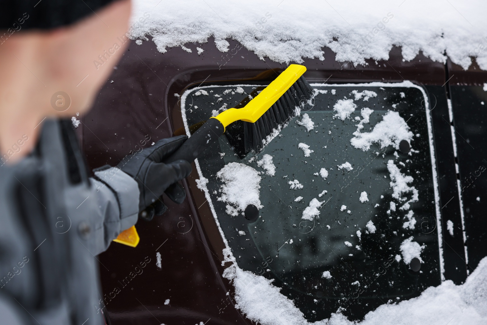 Photo of Man cleaning snow from car window outdoors, closeup