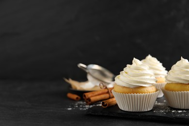 Photo of Delicious cupcakes with cream and cinnamon on black table. Space for text