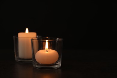 Photo of Burning candles in glass holders on table against dark background, space for text