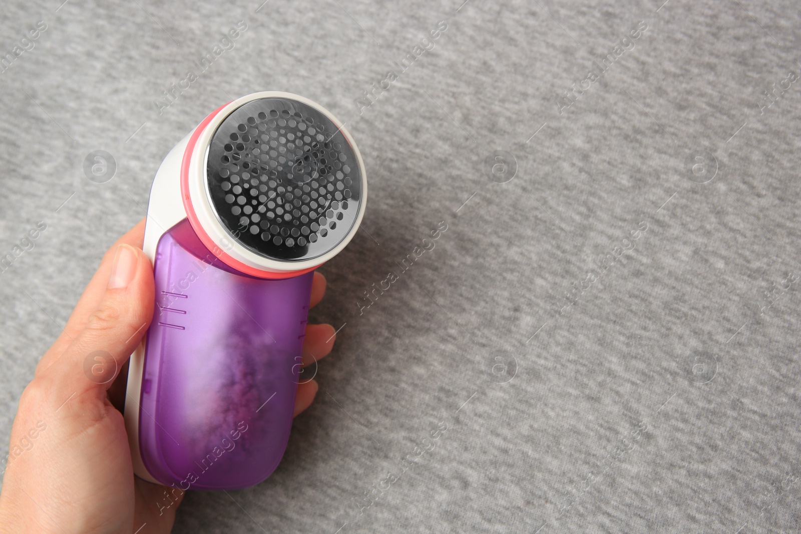 Photo of Woman holding fabric shaver near light grey cloth with lint, closeup. Space for text