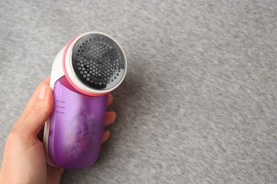 Woman holding fabric shaver near light grey cloth with lint, closeup. Space for text