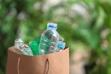 Photo of Paper bag with used plastic bottles and space for text on blurred background. Recycling problem