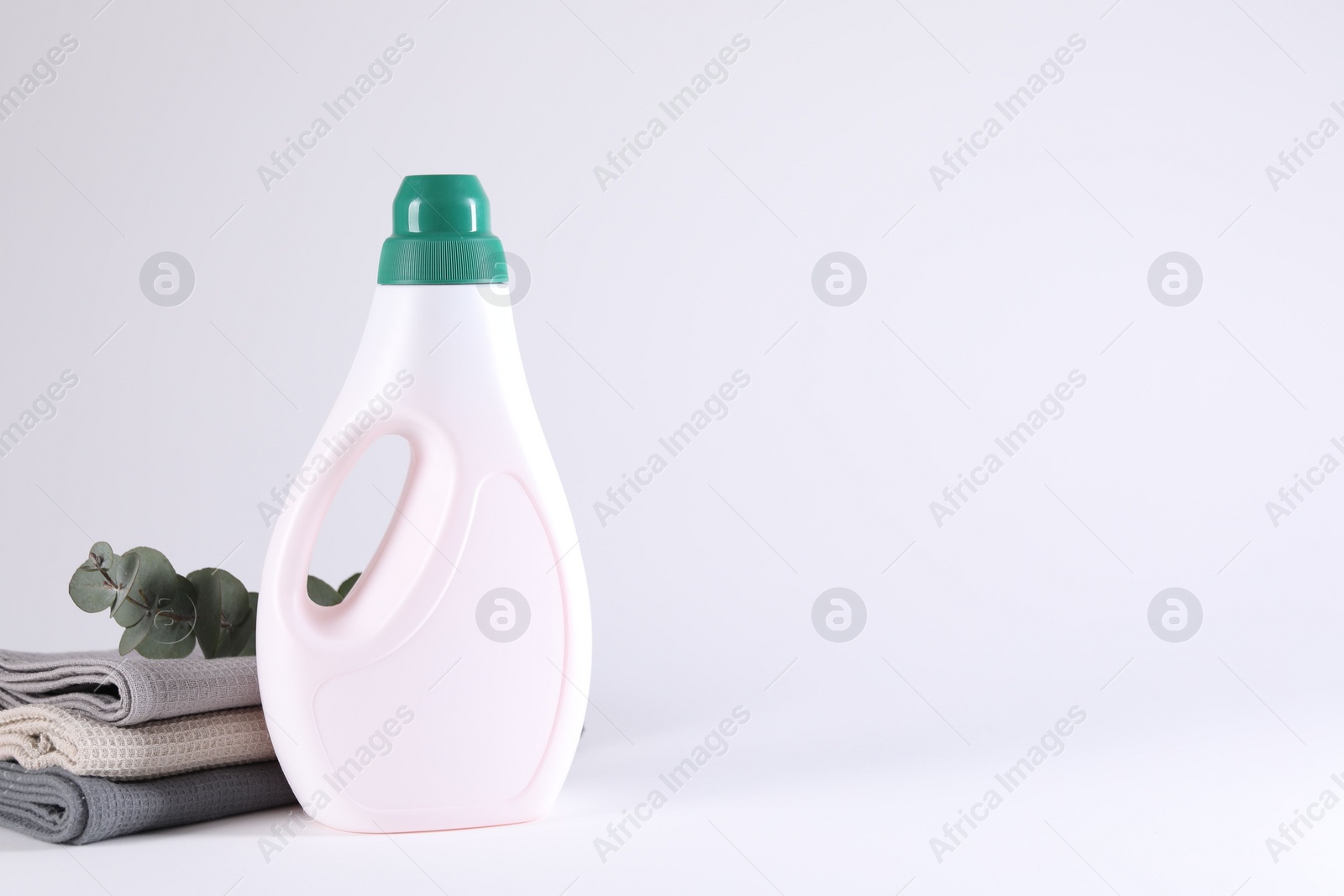 Photo of Bottle of cleaning product, rags and floral decor on light background