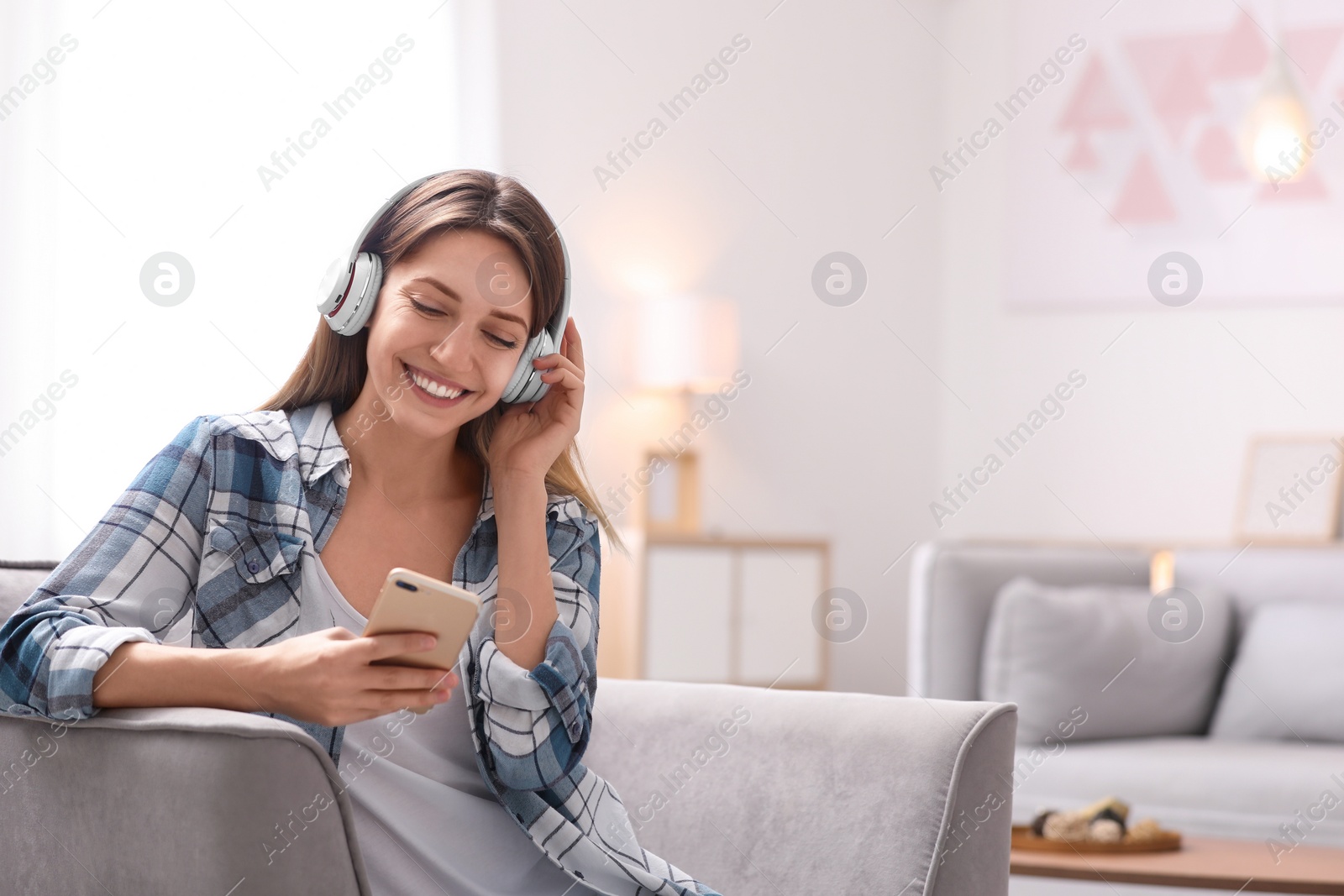 Photo of Young woman with headphones and mobile device resting in armchair at home