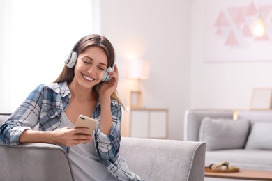 Photo of Young woman with headphones and mobile device resting in armchair at home