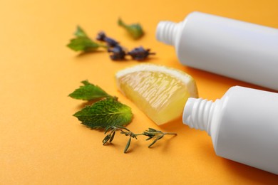 Photo of Blank tubes of toothpaste with mint, lemon and thyme on orange background, closeup
