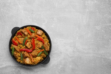 Serving pan of delicious rice with chicken and vegetables on light grey table, top view. Space for text