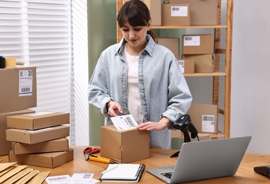 Parcel packing. Post office worker sticking barcode on box at wooden table indoors