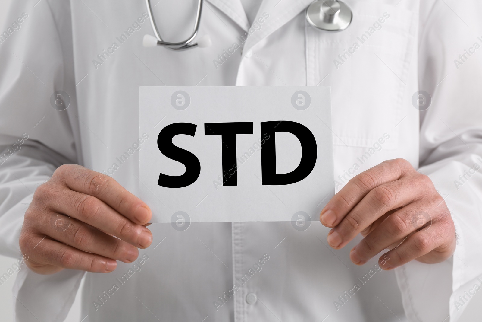 Photo of Doctor holding sheet of paper with abbreviation STD on white background, closeup