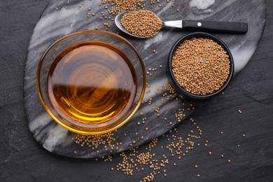 Photo of Bowl of natural oil and mustard seeds on black table, flat lay