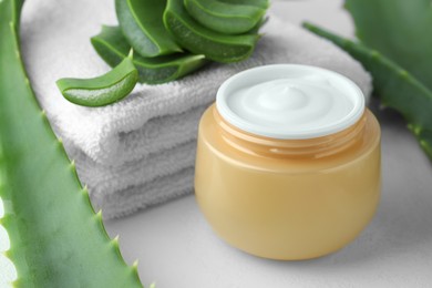 Jar with cream, cut aloe leaves and towel on white table, closeup