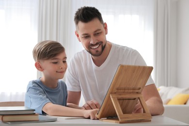 Photo of Boy with father doing homework using tablet at table in living room