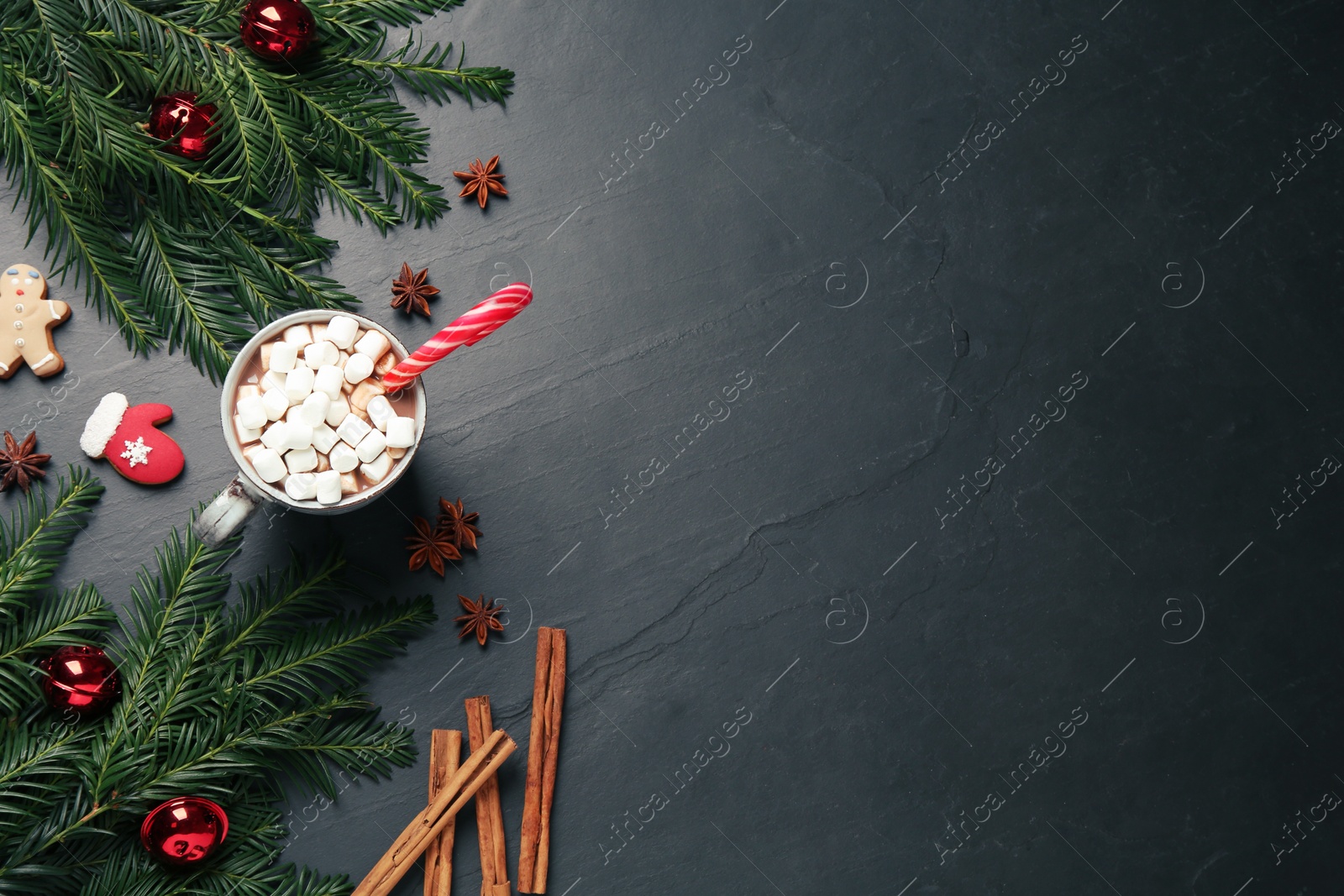 Photo of Delicious hot chocolate with marshmallows and candy cane near Christmas decor on black table, flat lay. Space for text