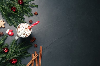 Delicious hot chocolate with marshmallows and candy cane near Christmas decor on black table, flat lay. Space for text