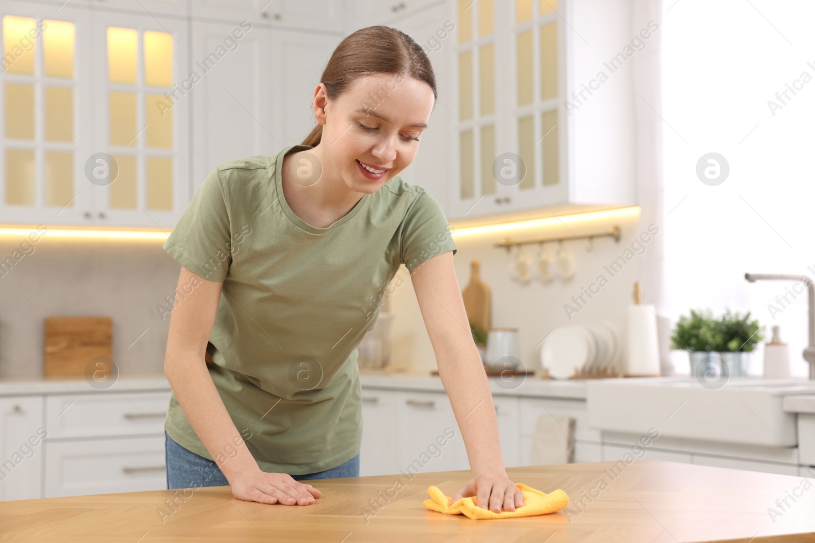 Photo of Woman with microfiber cloth cleaning wooden table in kitchen