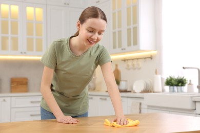 Woman with microfiber cloth cleaning wooden table in kitchen