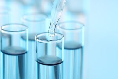 Photo of Dripping liquid from pipette into test tube on light blue background, closeup