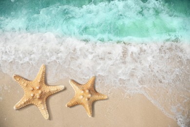 Image of Beautiful waves and sea stars on sandy beach, top view