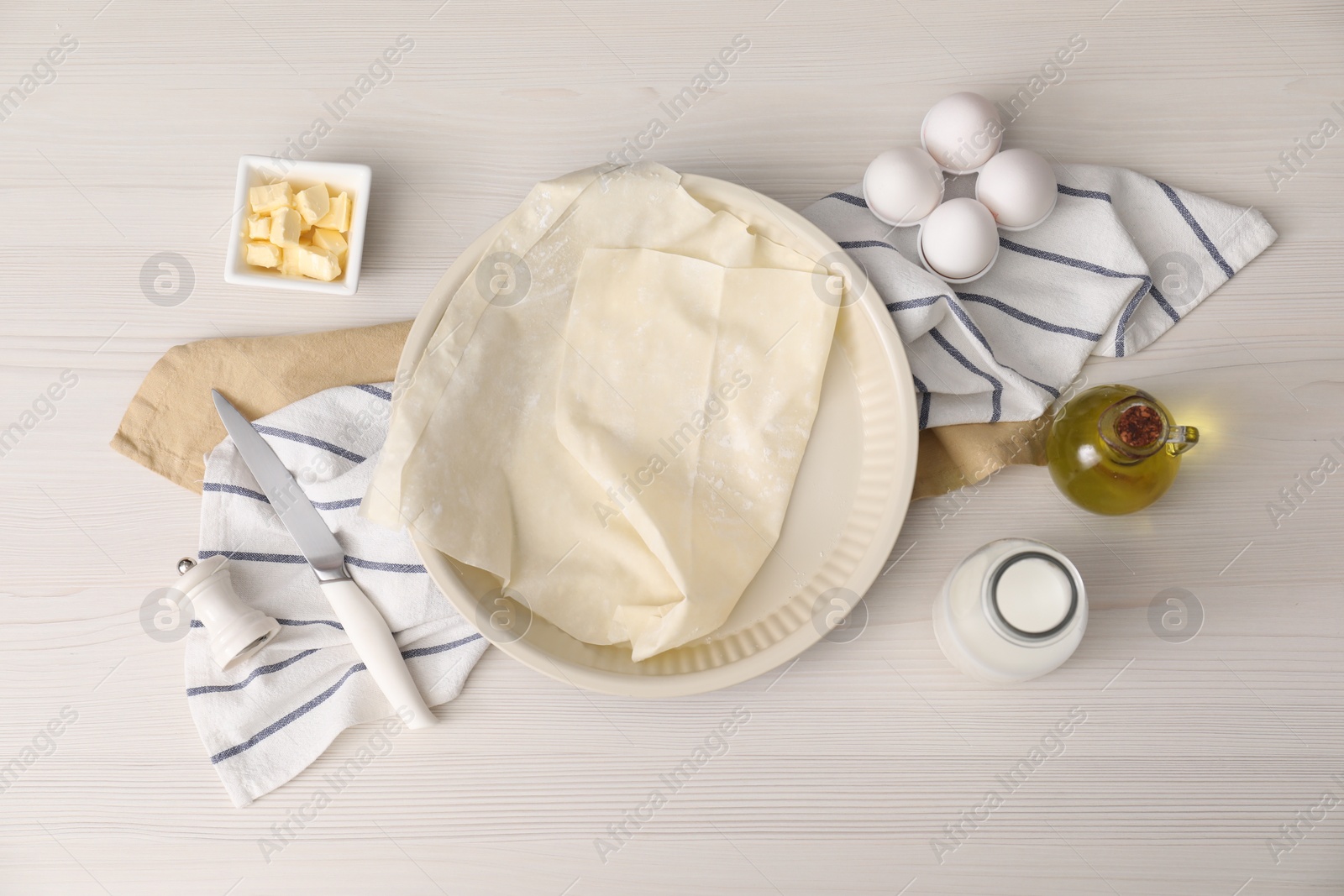 Photo of Fresh dough and different ingredients for making baklava on white wooden table, flat lay