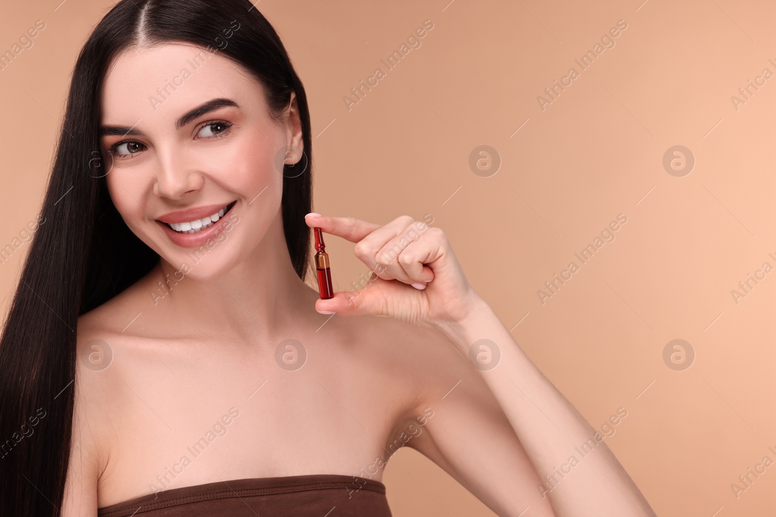 Photo of Beautiful young woman holding skincare ampoule on beige background. Space for text