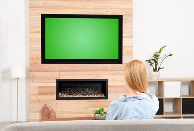 Photo of Woman watching TV on sofa in living room with decorative fireplace