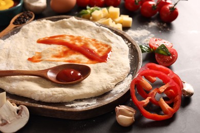 Photo of Pizza dough with tomato sauce and products on dark table, closeup