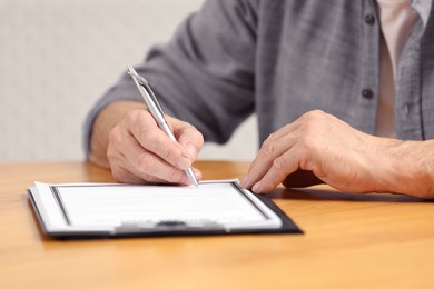 Senior man signing Last Will and Testament at wooden table indoors, closeup