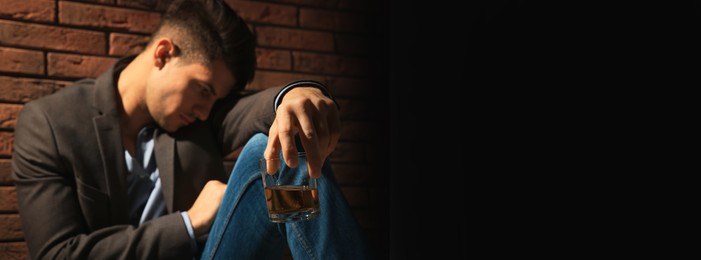 Suffering from hangover. Man with glass of alcoholic drink near red brick wall, selective focus. Banner design with space for text