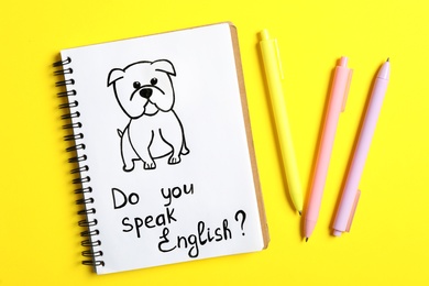 Photo of Notebook with question Do You Speak English and pens on yellow background, flat lay