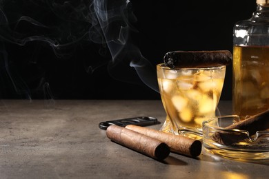 Photo of Cigars, ashtray, whiskey and cutter on grey table against black background. Space for text