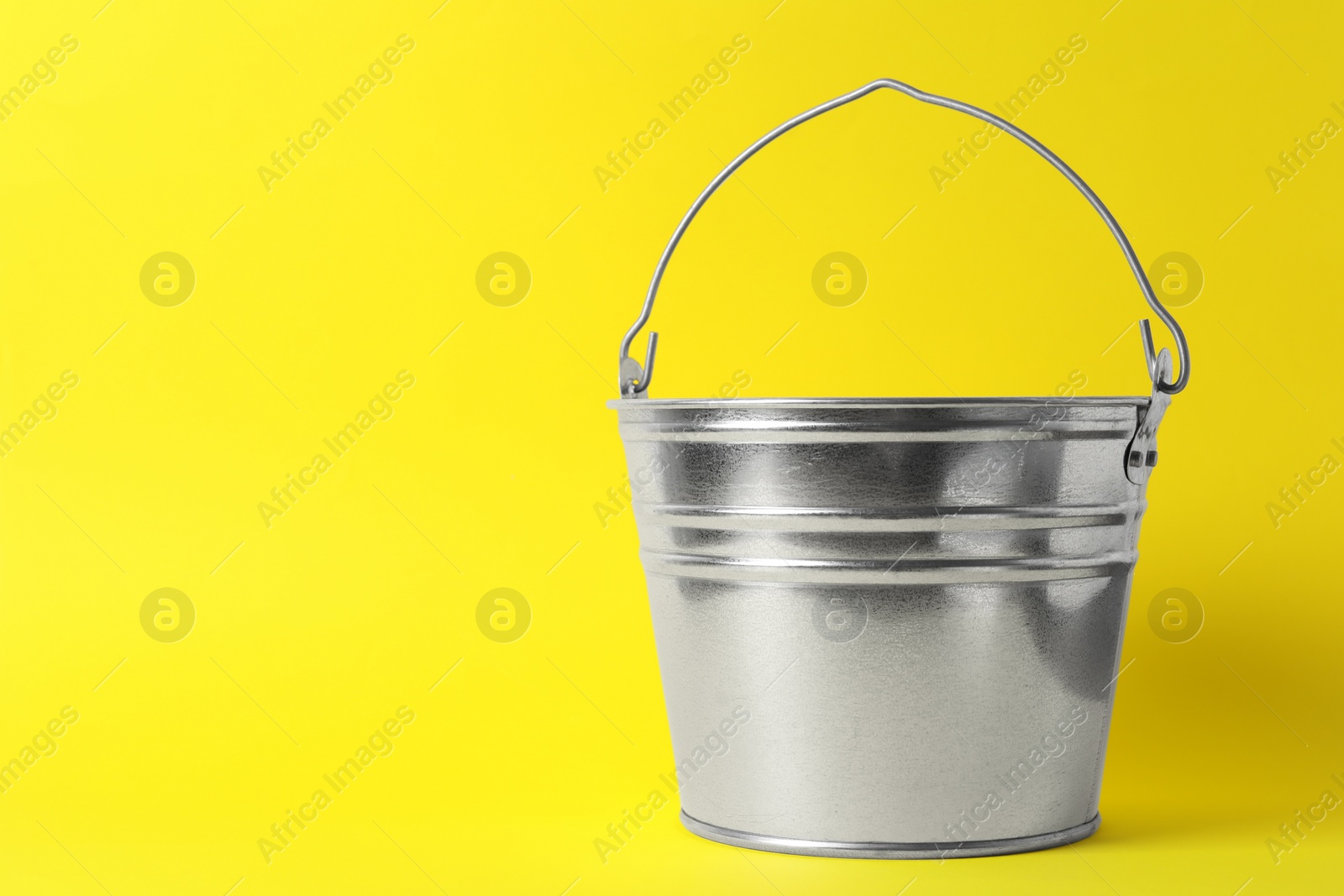 Photo of One shiny metal bucket on yellow background. Space for text