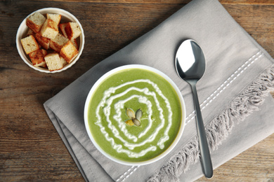 Delicious broccoli cream soup served on wooden table, flat lay