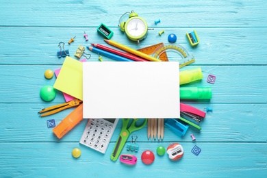 Flat lay composition with blank card and different school stationery on light blue wooden table. Space for text