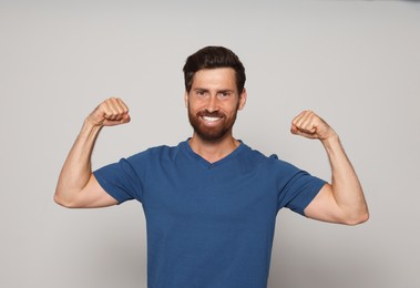 Photo of Smiling bearded man showing biceps on grey background
