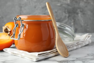Photo of Delicious persimmon jam and fresh fruits on white marble table, closeup