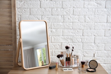 Photo of Makeup cosmetic products and tools on dressing table near brick wall with space for text