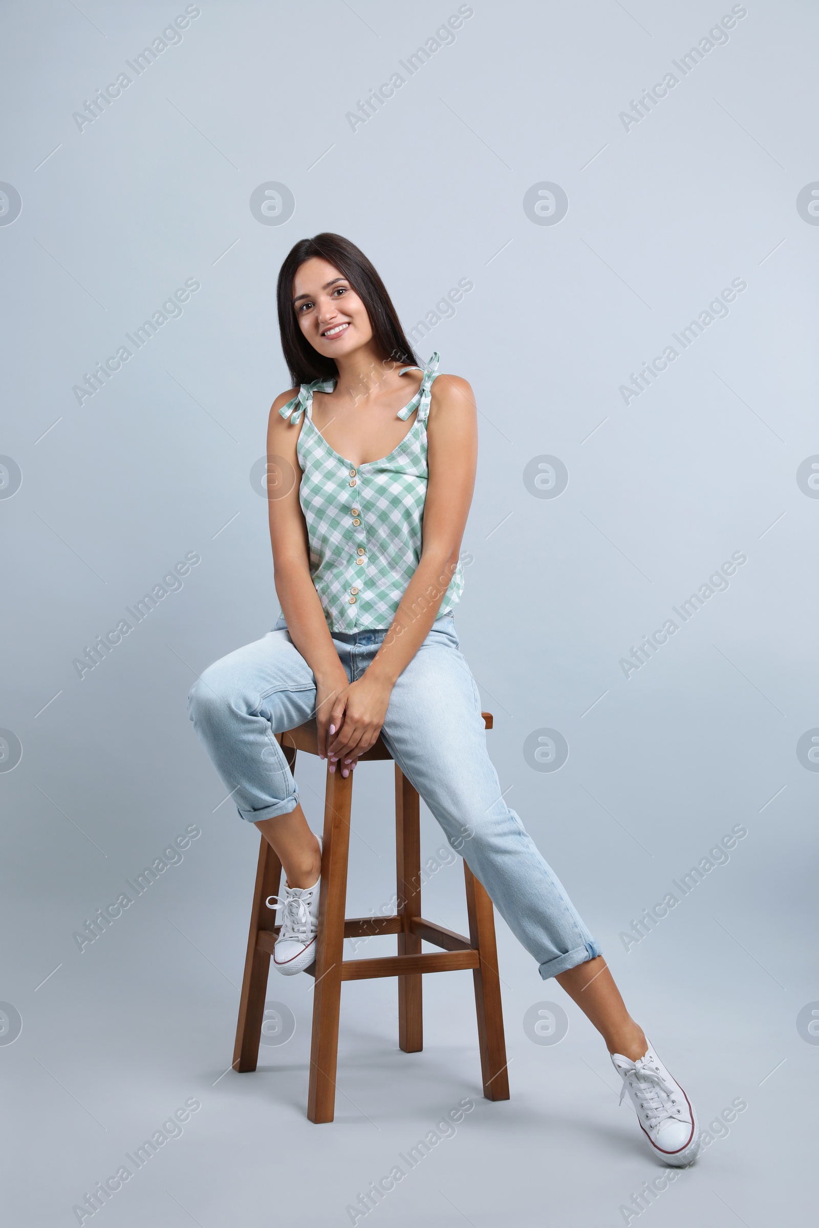 Photo of Beautiful young woman sitting on stool against light grey background