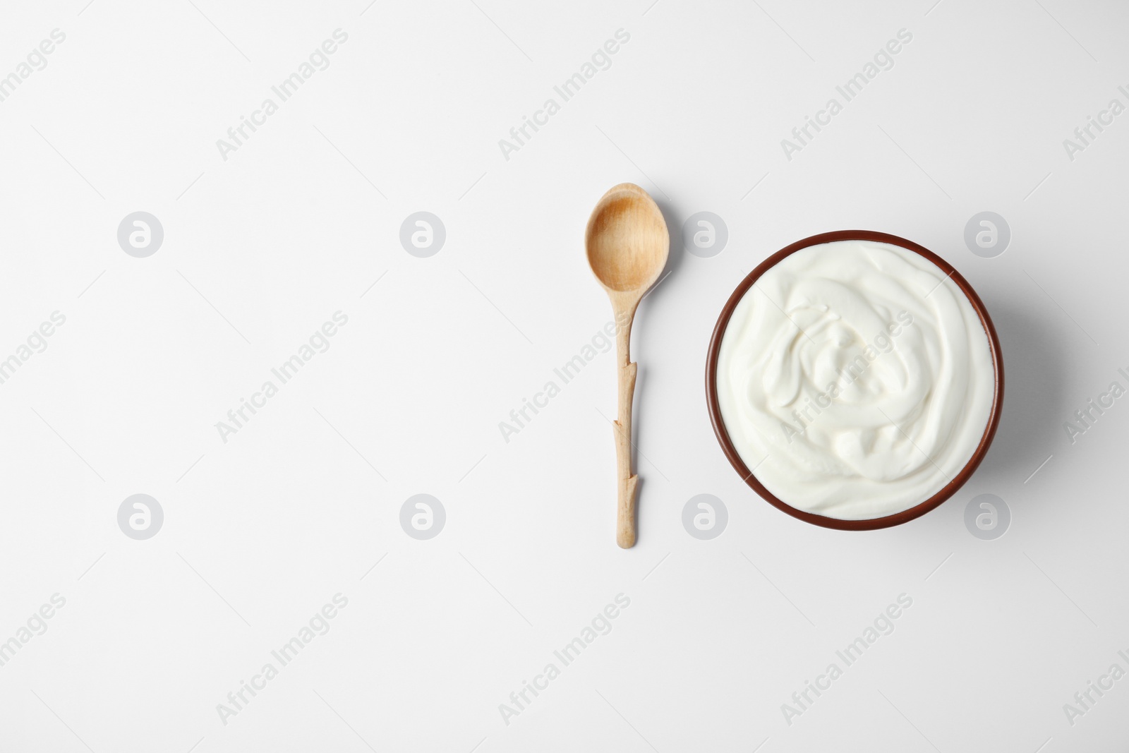 Photo of Bowl of sour cream and wooden spoon on white background, top view