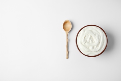 Photo of Bowl of sour cream and wooden spoon on white background, top view