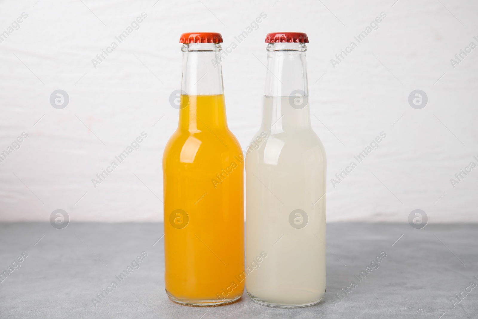 Photo of Delicious kombucha in glass bottles on grey table against white background