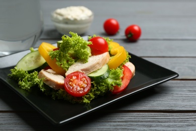 Delicious salad with chicken and vegetables on grey wooden table, closeup