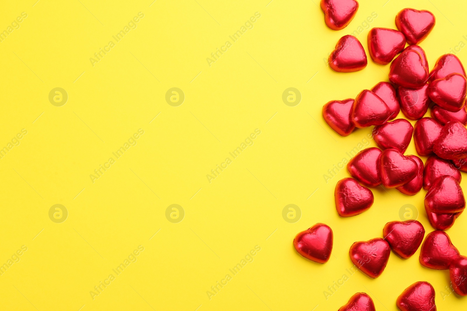 Photo of Heart shaped chocolate candies in red foil on yellow background, flat lay. Space for text